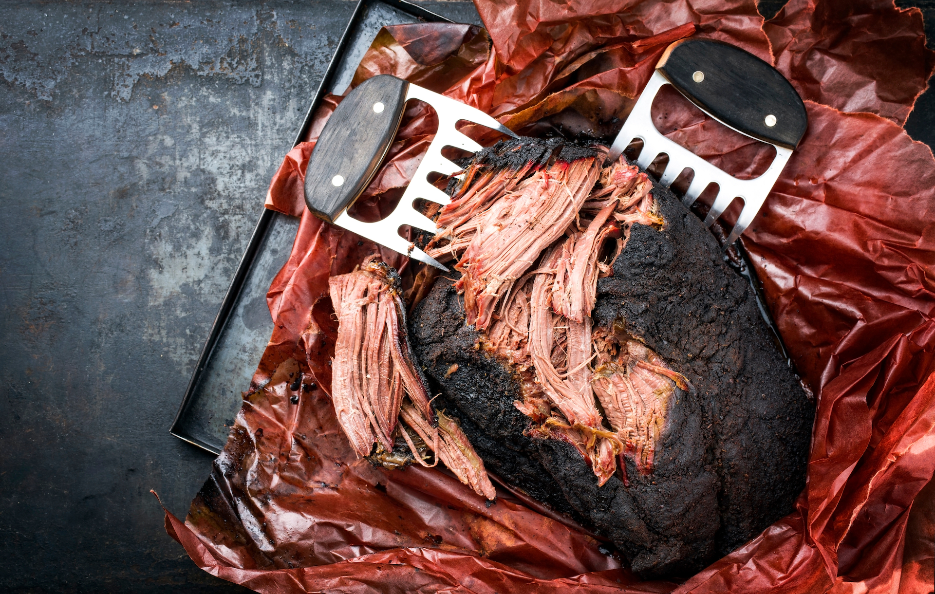 Traditional barbecue wagyu pulled beef in peach paper as top view with meat claws on a rustic board